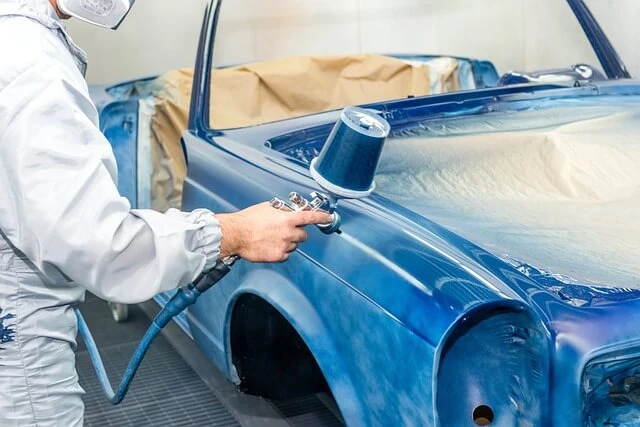 Auto Painting-man dressed in protective suit spraying blue paint on car