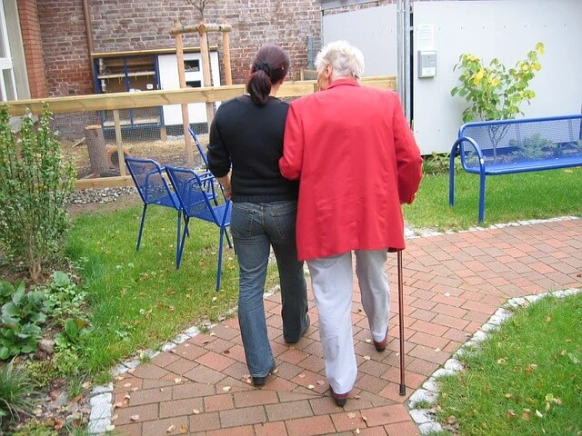 Caregiver Business - Young woman escorting older woman down brick pathway