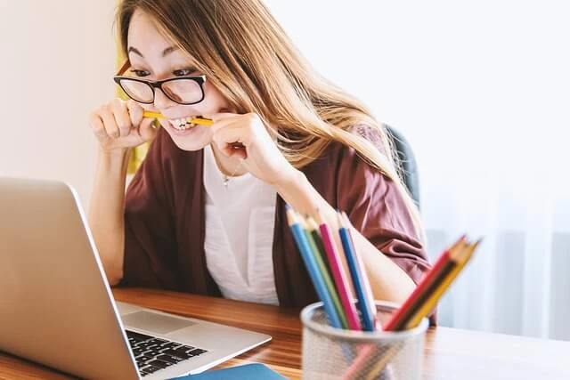 Charter School - young woman biting on pencil looking at laptop