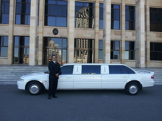 Limousine Service-White stretch limo outside office building with chauffeur waiting