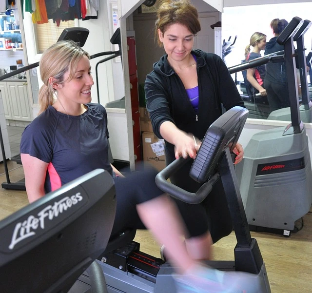 Personal Trainer -Trainer showing another woman how to operate cycle machine